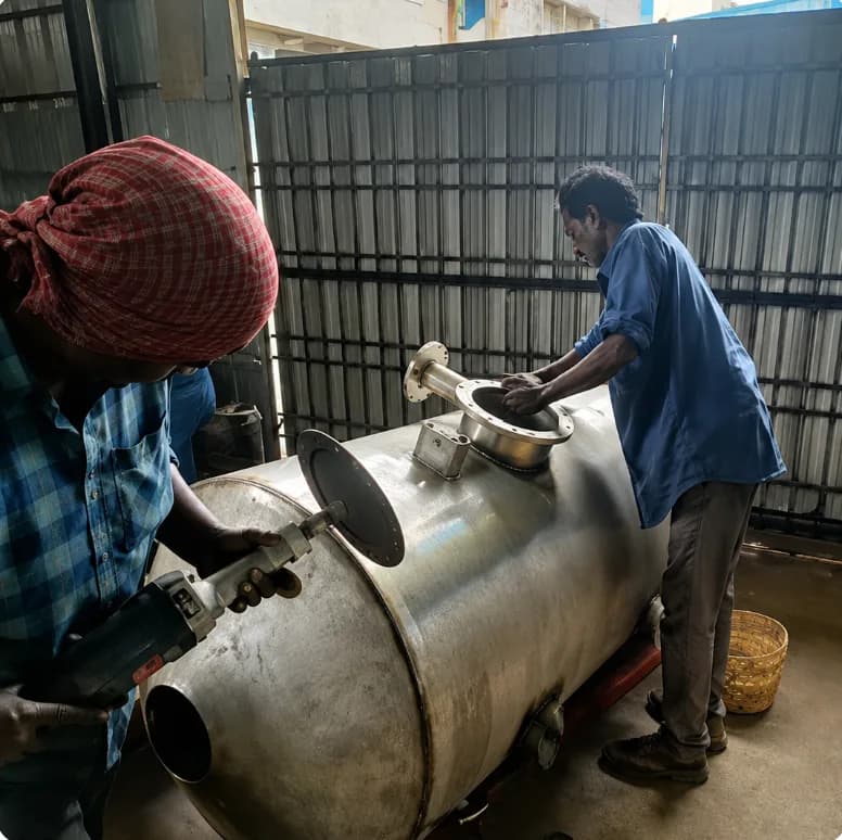 Two workers polishing and fitting flanges on a stainless steel tank