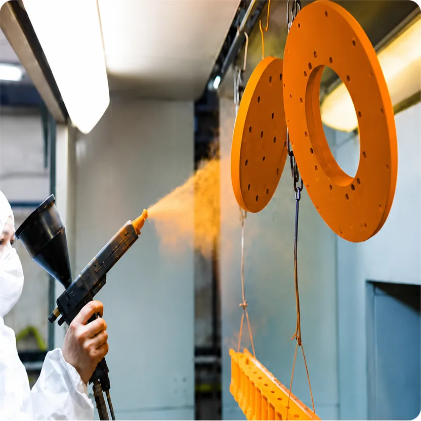 Operator electrostatically spraying orange powder coating onto hanging metal discs in a coating booth