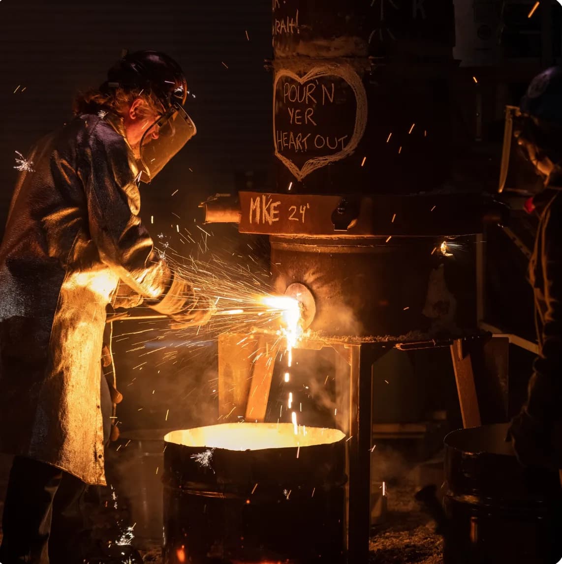 Foundry worker in protective gear pouring molten metal from a furnace