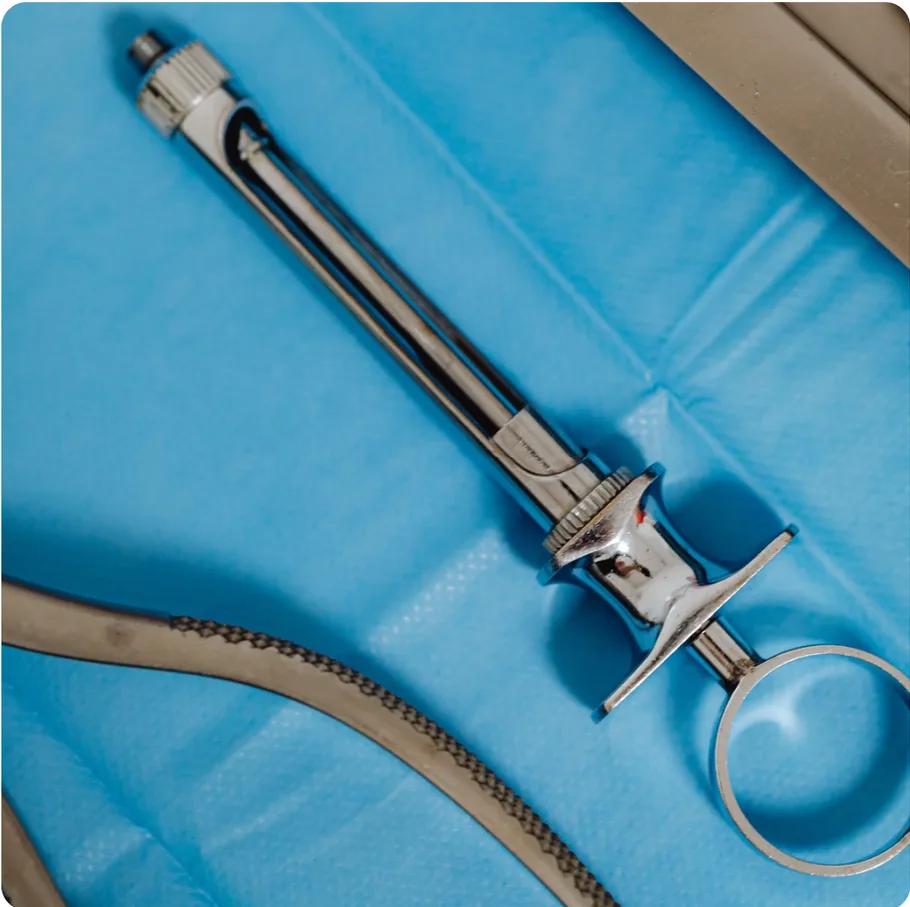 Stainless steel dental syringe resting on a blue sterile drape beside surgical instruments